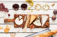 Red and white wine plus different kinds of cheeses (cheeseboard) on rustic wooden table. French food tasting party or feast scenery from above (top view).